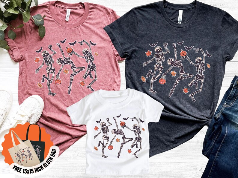 May include: Three t-shirts in various colours, including a dusty rose, charcoal, and white, each with a dancing skeleton design with pumpkins and bats. A free 38x38 cm cloth bag with the same design is also included.