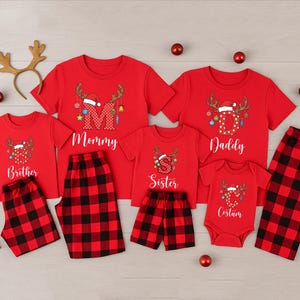 May include: Red Christmas family pajama sets with matching plaid bottoms. Each shirt features a reindeer design with a Santa hat and the words "Mommy", "Daddy", "Brother", "Sister", and "Cousin". Includes a reindeer antler headband and red ornaments.