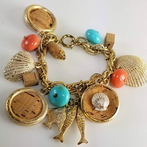 May include: A gold charm bracelet with a variety of charms, including seashells, fish, and cork circles. The charms are attached to a gold chain with a lobster clasp.