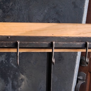 Op de afbeelding: Een zwarte metalen rek met vijf haken gemonteerd op een houten oppervlak. Het rek is ontworpen om keukengerei of andere items aan op te hangen.