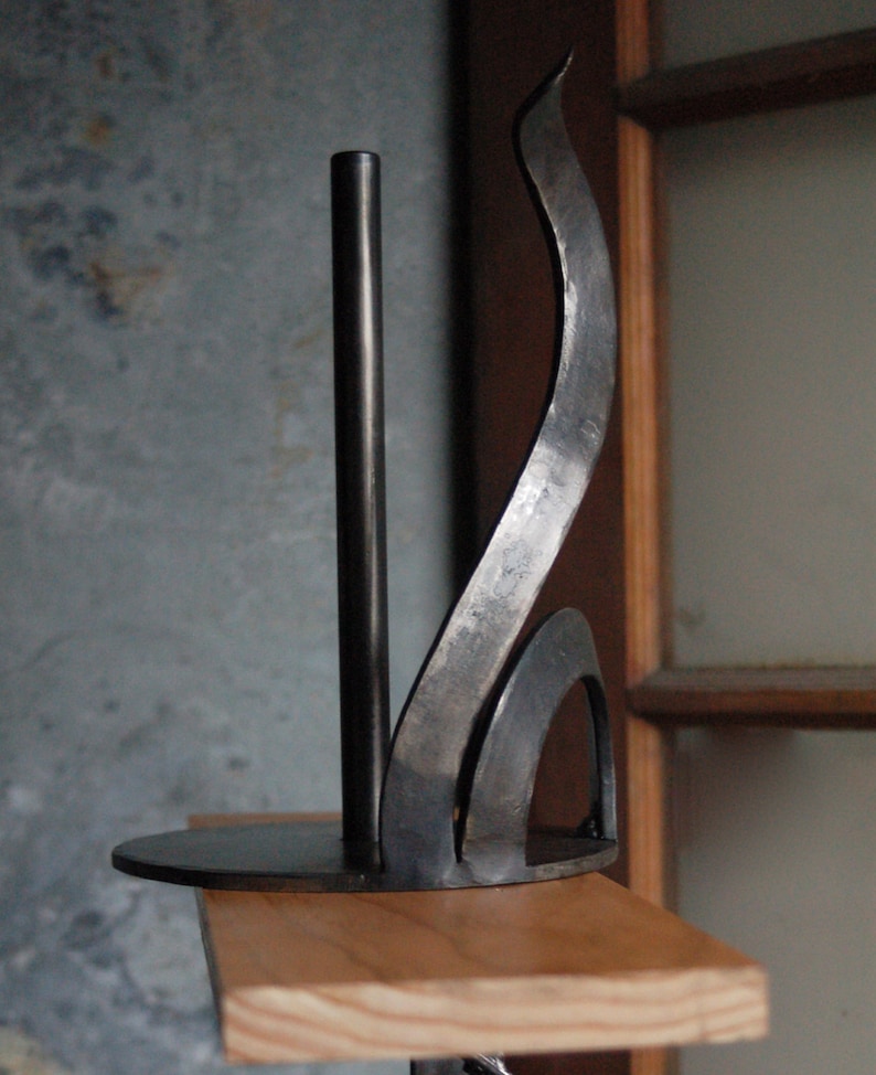 May include: A black metal paper towel holder with a curved design. The holder is mounted on a wooden shelf.