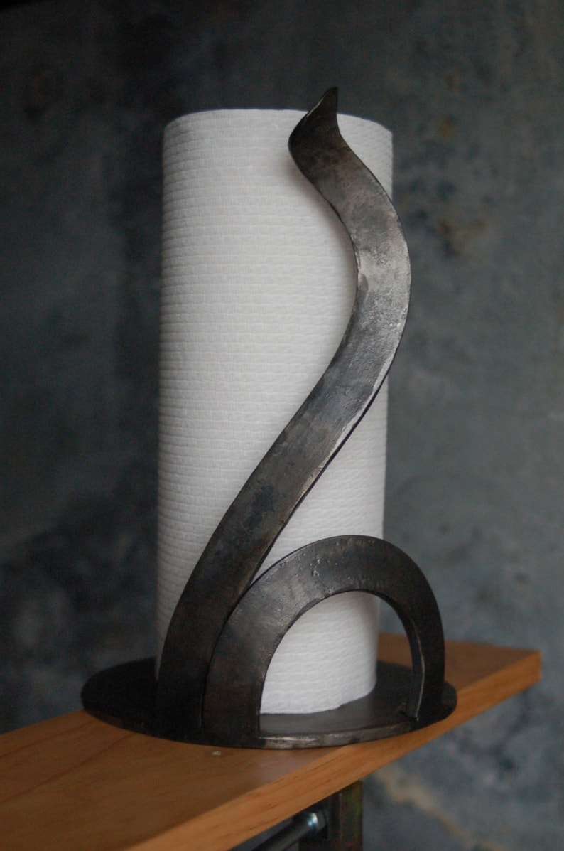 May include: A black metal paper towel holder with a curved design. The holder is made of a single piece of metal and has a simple, modern look.