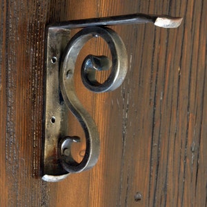May include: A metal shelf bracket with a decorative scroll design. The bracket is made of dark metal and has a rustic finish.