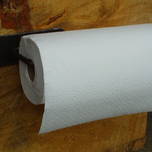 May include: Black metal paper towel holder mounted on a wooden wall with a white paper towel roll attached.
