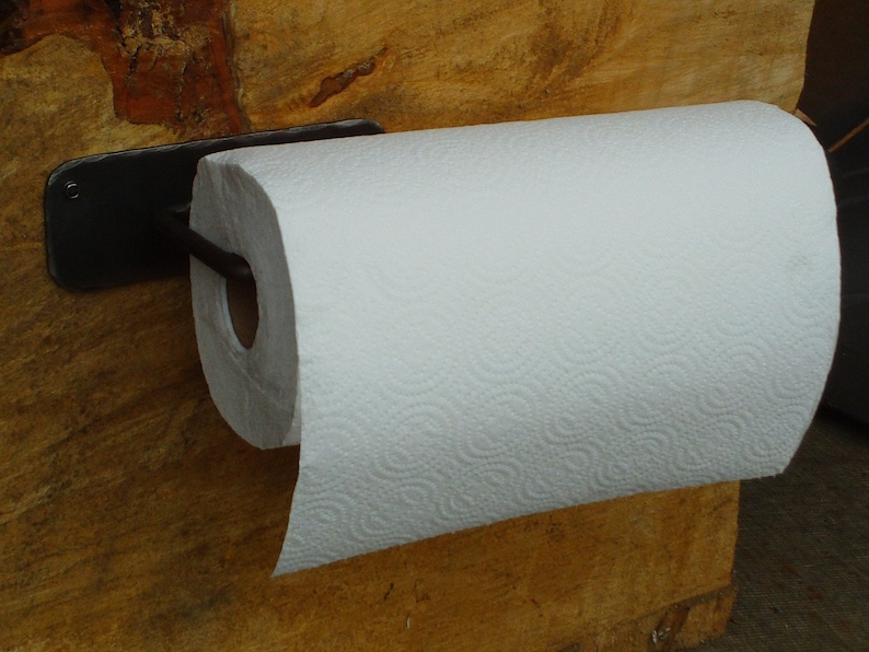 May include: Black metal paper towel holder mounted on a wooden wall with a white paper towel roll attached.