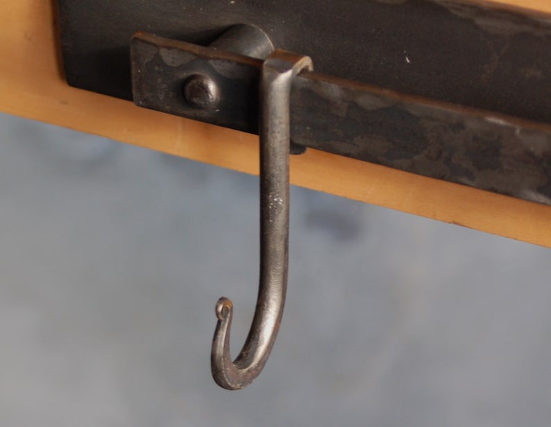 Op de afbeelding: Een zwarte metalen haak met een gebogen uiteinde, bevestigd aan een zwarte metalen balk.