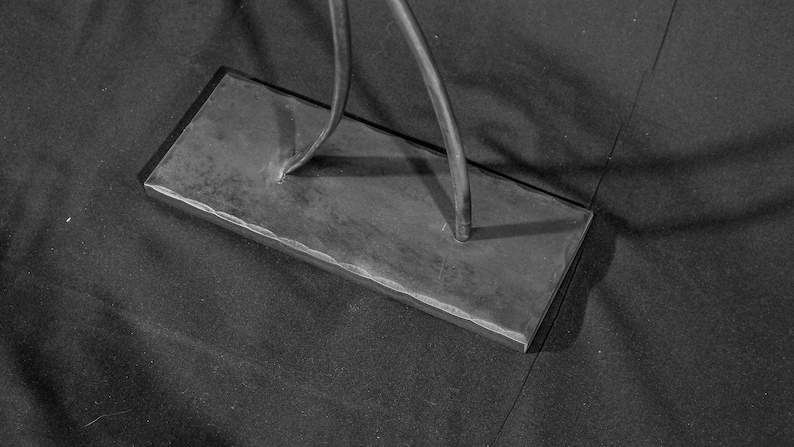 May include: A black metal base with a textured surface. Two metal rods are attached to the base.