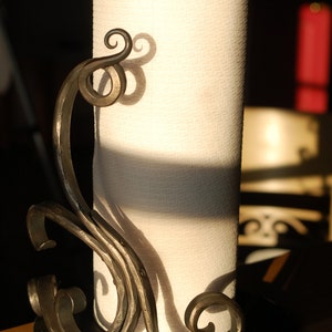 May include: A black metal paper towel holder with a decorative scroll design. The holder is holding a roll of white paper towels.