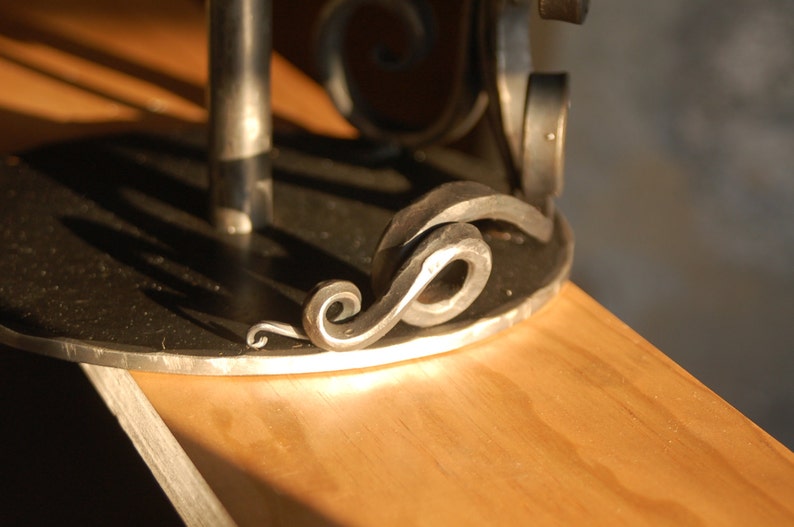 May include: A black metal base with a decorative scroll design. The base is made of wrought iron and has a smooth, polished finish.