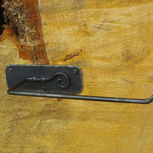 May include: A black metal toilet paper holder with a decorative scroll design. The holder is mounted on a wooden surface.