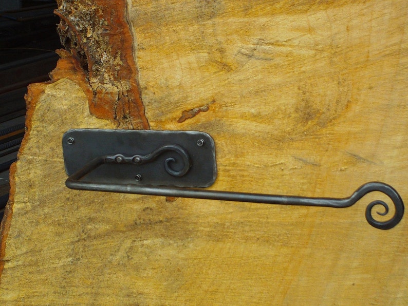 May include: A black metal toilet paper holder with a decorative scroll design. The holder is mounted on a wooden surface.