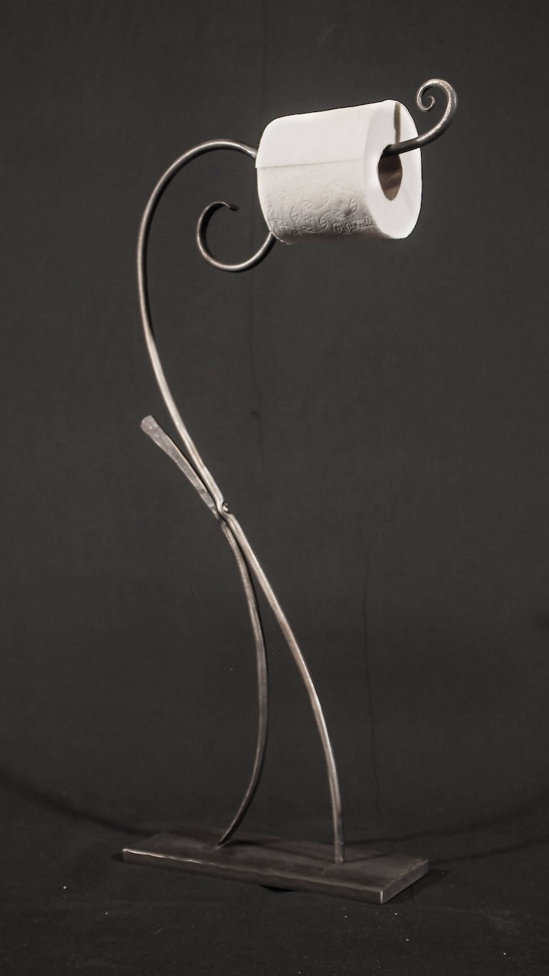 May include: A black metal toilet paper holder with a decorative scroll design. The holder is freestanding and has a base.