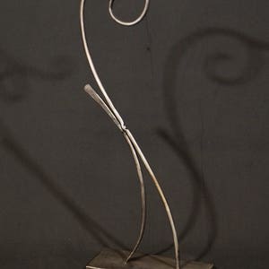 May include: A metal sculpture with a unique, abstract design. The sculpture is made of two pieces of metal that are bent and twisted into a flowing, organic shape. The sculpture is mounted on a rectangular base.