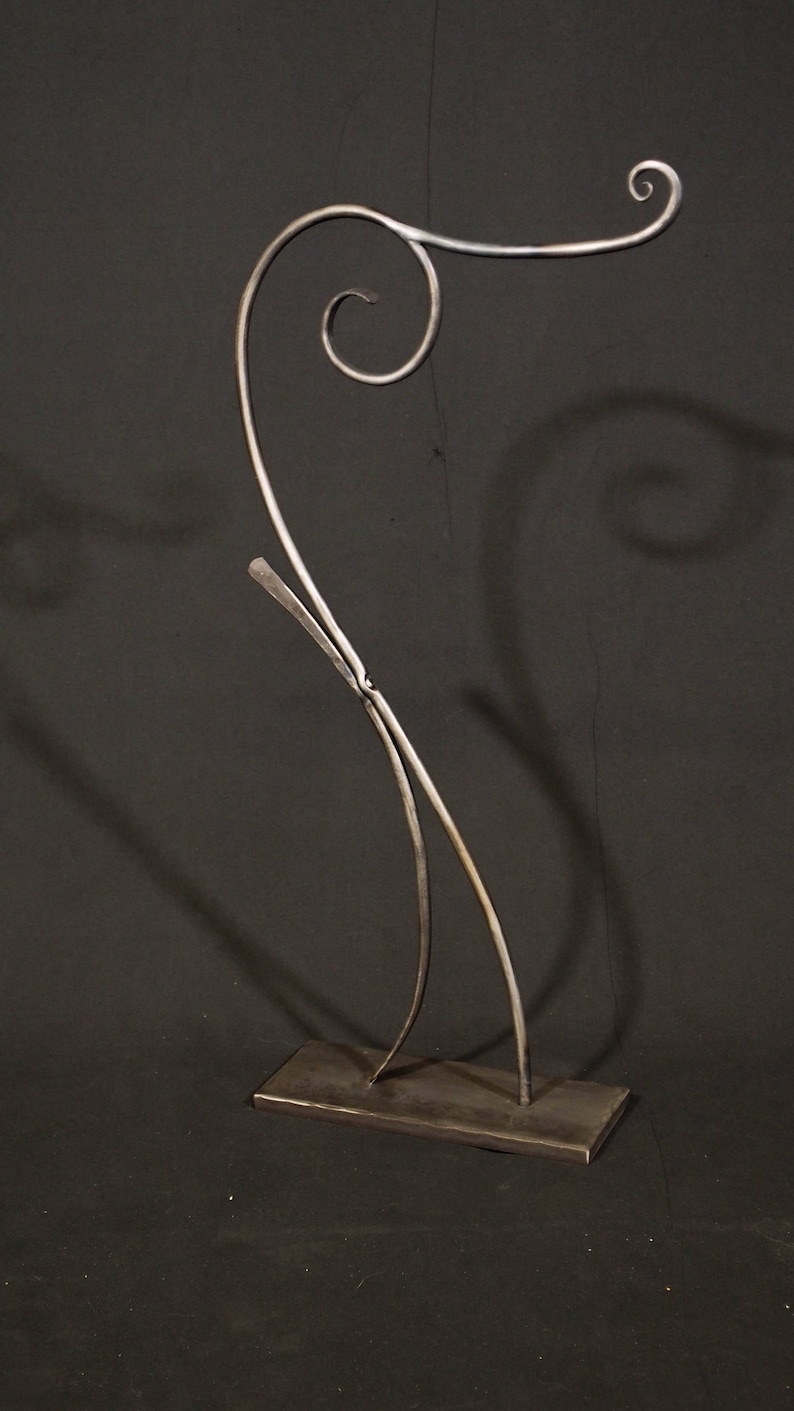 May include: A metal sculpture with a unique, abstract design. The sculpture is made of two pieces of metal that are bent and twisted into a flowing, organic shape. The sculpture is mounted on a rectangular base.