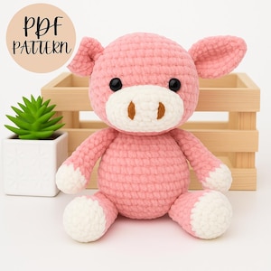 May include: A handmade pink crochet pig with black eyes, a white snout, and white accents on its feet. The pig is sitting in front of a wooden crate and a small potted succulent. The text "PDF PATTERN" is in a circle in the upper left corner.