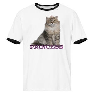 May include: White t-shirt with black trim featuring a graphic of a fluffy cat wearing a crown and necklace. The word "PRINCESS" is printed in purple below the cat.