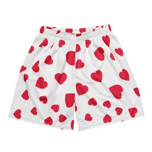 Może przedstawiać: Białe szorty sportowe z powtarzającym się wzorem czerwonych serc. Szorty mają elastyczny pas i luźny krój, odpowiednie do noszenia na co dzień lub na treningi. Kształty serc różnią się wielkością i są równomiernie rozłożone.