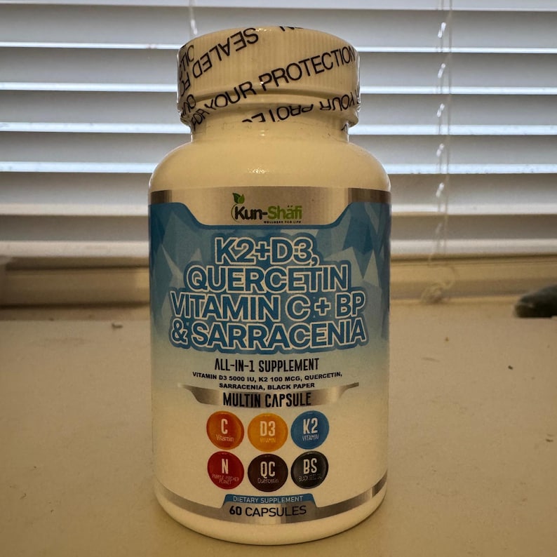 K&ouml;nnte beinhalten: Eine wei&szlig;e Erg&auml;nzungsflasche mit einem blau-wei&szlig;en Etikett. Das Etikett enth&auml;lt den Text "K2+D3, Quercetin, Vitamin C+BP & Sarracenia" und "All-in-1-Erg&auml;nzungsmittel". Die Flasche ist mit einem wei&szlig;en Deckel versiegelt, auf dem "F&uuml;r Ihren Schutz" steht. Die Flasche enth&auml;lt 60 Kapseln.