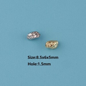 May include: Two textured metal beads, one silver and one gold, on a blue background. The silver bead is on the left, and the gold bead is on the right. The beads are approximately 8.5x6x5mm in size with a 1.5mm hole.