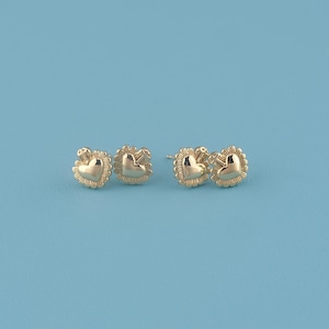 Peut inclure: Quatre boucles d'oreilles à clous dorées en forme de cœur. Chaque cœur est entouré d'un motif détaillé en forme d'éclat de soleil. Les boucles d'oreilles sont présentées sur un fond bleu clair, mettant en valeur leurs détails.