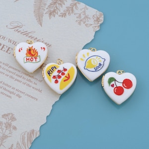 May include: Four white heart-shaped metal lockets with gold-tone edges. The first features a flame graphic and the word HOT. The second shows a tomato vine and the word RIPE. The third displays a lemon graphic and the word SOUR. The fourth shows cherries.