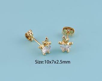 May include: A pair of gold-colored stud earrings with a leaf design and a clear, oval-shaped stone. The earrings are 10mm x 7mm x 2.5mm in size. The earrings are displayed on a light blue background.