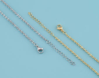 May include: Close-up of three delicate necklaces in silver and gold tones against a light blue background. The necklaces feature different chain styles, including a twisted rope design and a classic link chain. Each necklace has an adjustable extender.