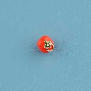 May include: A small, glossy, orange tomato charm with a gold-coloured ring and green leaf detail. The charm is set against a light blue background, creating a vibrant contrast. This charm is suitable for jewellery making.