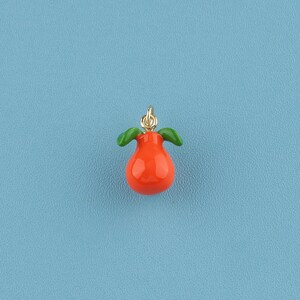 May include: A small, orange pear-shaped charm with two green leaves and a gold-coloured loop for hanging. The charm is set against a light blue background.