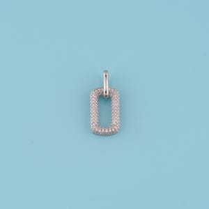 May include: A silver-toned pendant with a rectangular shape, encrusted with small, clear gemstones. The pendant has a small loop at the top for a chain. The background is a solid light blue.