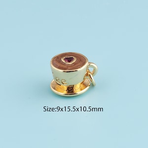 Puede incluir: Un dije dorado con forma de taza de café con platillo. La taza de café tiene un interior marrón con una gema en forma de corazón. El dije mide 0,9x1,55x1,05cm.