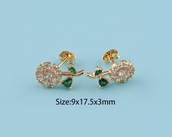 May include: A pair of gold-toned stud earrings. Each earring features a flower design with clear crystals and green accents, along with a stem and leaf detail. The earrings measure 9x17.5x3mm.