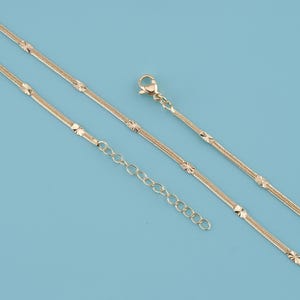 May include: Gold-colored necklace with a delicate chain design. The necklace features a series of starburst-shaped accents along the chain and an adjustable length. The clasp and extender chain are also gold-toned, set against a light blue background.