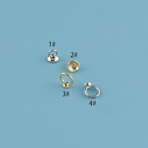 Peut inclure: Quatre apprêts de bijoux métalliques sont présentés sur un fond bleu. Les apprêts comprennent une bague argentée avec une petite boule, une bague dorée avec une boule, un apprêt en forme de coupe dorée et un apprêt argenté avec une base plate.