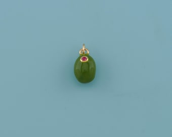May include: A green olive-shaped pendant with a small red gemstone and a gold-colored bail. The pendant is set against a light blue background. This jewelry item is a unique accessory.