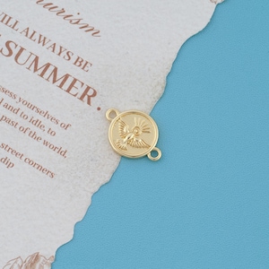 May include: A circular gold-toned metal charm featuring a relief design of a dove with outstretched wings and radiating sunbeams above it. The charm has two small loops on opposite sides for attachment, creating a connector piece for jewellery.