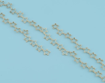 Op de afbeelding: Goudkleurige sterrenketting op een lichtblauwe achtergrond. De ketting bestaat uit verbonden stervormige schakels, waardoor een delicaat ontwerp ontstaat. De kettingen zijn in een trapsgewijs patroon gerangschikt.