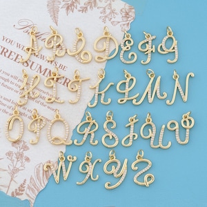 May include: A collection of twenty-six gold-toned metal letter charms, each featuring a cursive script design embellished with small, clear white stones along the front surface. Each individual letter charm includes a small loop at the top.