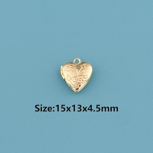 May include: A gold-colored heart-shaped locket with floral detailing. The locket is 15mm x 13mm x 4.5mm and has a small loop at the top for attaching to a chain. The locket is on a blue background.