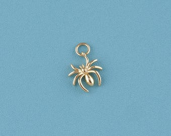 May include: A gold-colored spider charm with a loop at the top for hanging. The spider has eight legs and a rounded body. The charm is set against a solid blue background.