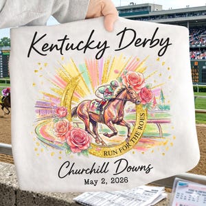 May include: White tote bag featuring a horse racing scene with a jockey, roses, and a horseshoe design. Text includes "Kentucky Derby", "Churchill Downs", and "May 2, 2026". The background shows a racetrack and spectators.
