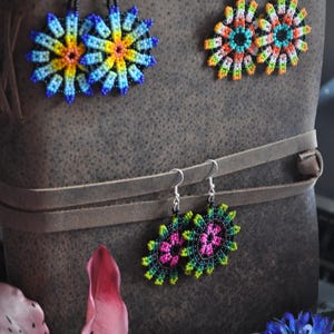 May include: Three pairs of beaded earrings in various floral designs. One pair is blue, yellow, and orange. Another is orange, green, and turquoise. The third pair is pink and green. All have silver hooks.