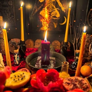 May include: A mystical scene featuring a central burning red candle with a tall flame, surrounded by lit yellow candles in black holders. The scene includes a red velvet surface, fruit, and a Baphomet image in the background.