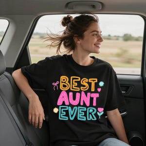 May include: A black short-sleeved t-shirt featuring the text BEST AUNT EVER in orange, pink, and teal bubble letters. The design includes small graphic illustrations of a pink bow, a teal flower, a pink heart, a yellow flower, and a pink tulip.