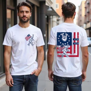 Peut inclure: T-shirt blanc avec un motif de Bigfoot tenant un drapeau américain et faisant un signe de la main rock and roll. Le dos du t-shirt présente un motif de drapeau américain vieilli avec les années 1776 et 2026.