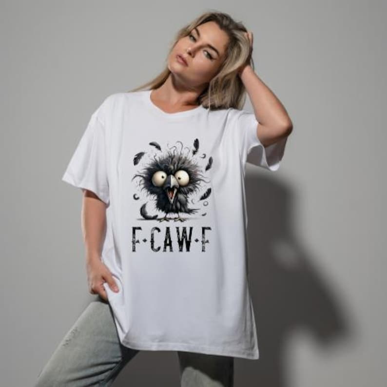 May include: White t-shirt featuring a cartoon crow with large eyes and scattered feathers. The crow graphic is black and gray, with the text "F-CAW-F" printed below. The shirt is a casual, short-sleeved style.