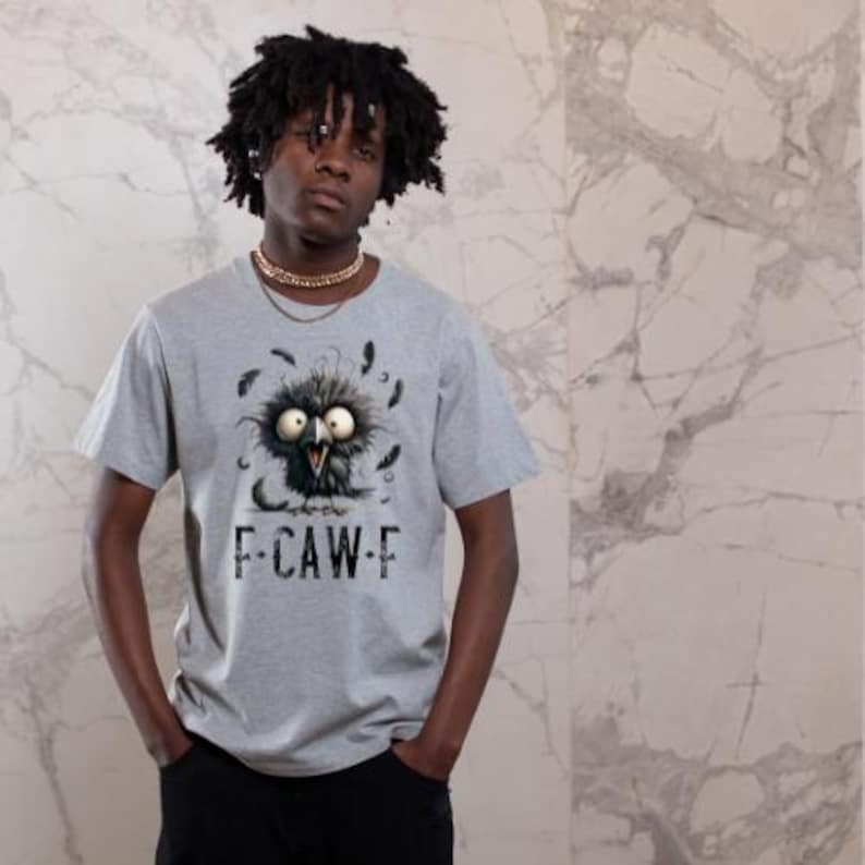 May include: A gray t-shirt featuring a cartoon crow with large eyes and feathers. The text "F-CAW-F" is printed below the crow. The shirt is short-sleeved.