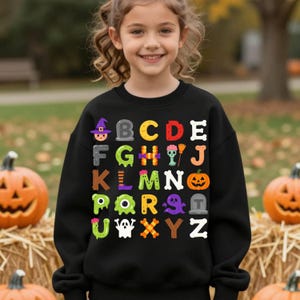 Peut inclure: Un sweat-shirt noir à manches longues avec une impression graphique colorée de l'alphabet de A à Z. Chaque lettre est stylisée avec des éléments sur le thème d'Halloween, notamment un chapeau de sorcière, une pierre tombale, une citrouille, un fantôme et divers os.