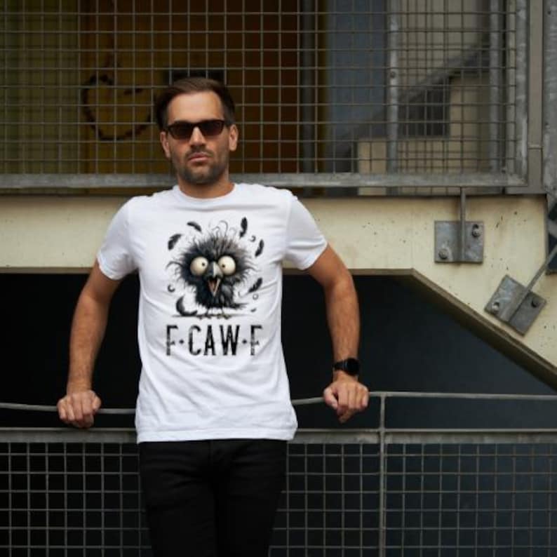 May include: White t-shirt featuring a cartoon bird with large eyes and feathers, with the text "F-CAW-F" printed below. The shirt is worn by a person wearing sunglasses and black pants.