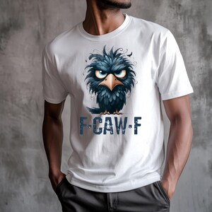 May include: White t-shirt featuring a cartoon illustration of a dark blue bird with an angry expression and a yellow beak. The text "F-CAW-F" is printed below the bird in blue. The shirt is made of a soft material.